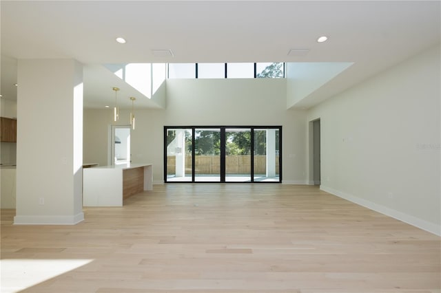 unfurnished living room with light hardwood / wood-style floors and a towering ceiling