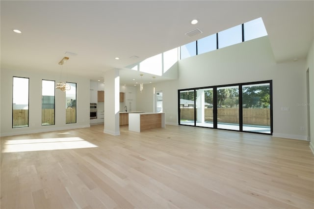 unfurnished living room featuring sink, light hardwood / wood-style flooring, a skylight, and a towering ceiling