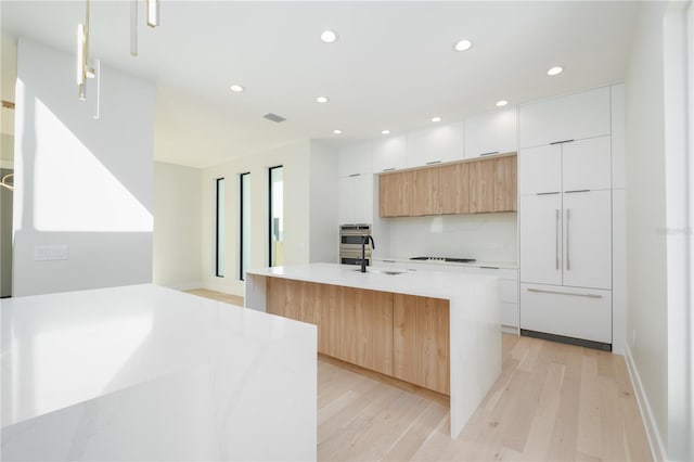 kitchen with light hardwood / wood-style flooring, white cabinetry, sink, a kitchen island with sink, and hanging light fixtures