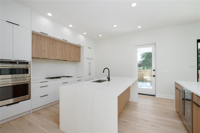 kitchen featuring sink, white cabinetry, double oven, and an island with sink