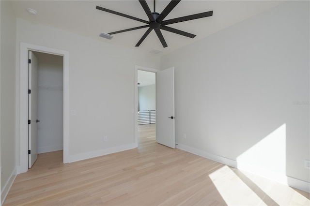 unfurnished bedroom featuring light wood-type flooring, a spacious closet, ceiling fan, and a closet