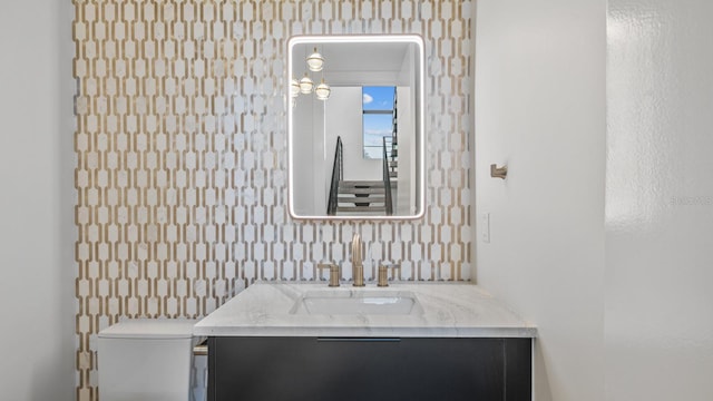 bathroom with vanity, toilet, and wallpapered walls