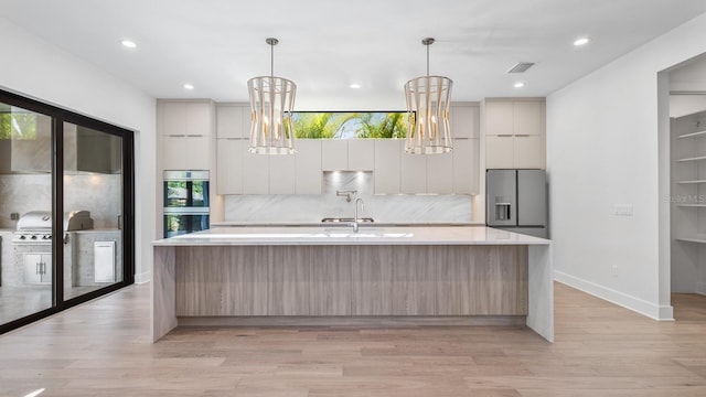 kitchen featuring stainless steel appliances, light countertops, a large island with sink, and modern cabinets