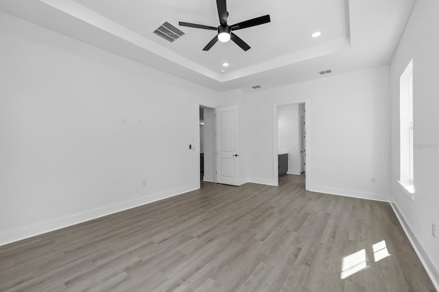 unfurnished bedroom with ceiling fan, light hardwood / wood-style flooring, and a tray ceiling