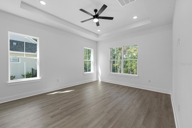 empty room with a raised ceiling, ceiling fan, and dark hardwood / wood-style flooring