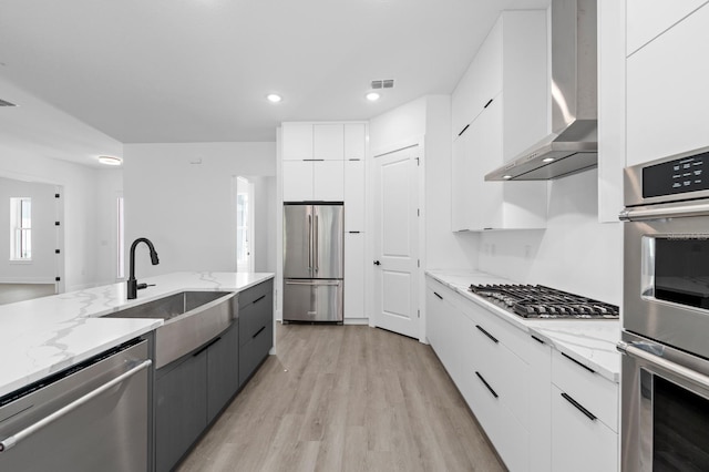 kitchen featuring white cabinets, appliances with stainless steel finishes, sink, and wall chimney range hood