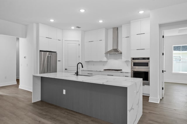 kitchen featuring white cabinetry, sink, wall chimney exhaust hood, a large island with sink, and appliances with stainless steel finishes