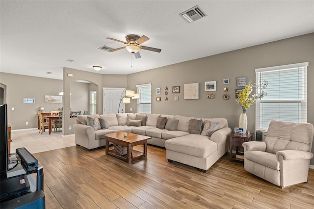 living room with ceiling fan, a textured ceiling, light hardwood / wood-style floors, and a healthy amount of sunlight