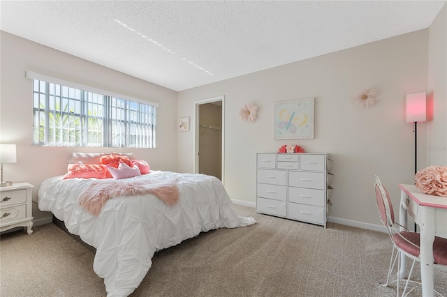 bedroom featuring a walk in closet, a textured ceiling, and light carpet