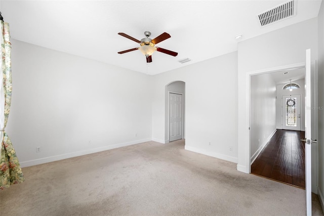 unfurnished room with carpet floors, visible vents, arched walkways, and a ceiling fan