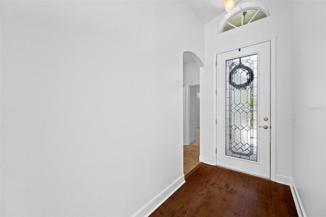 entryway with lofted ceiling, baseboards, arched walkways, and dark wood finished floors