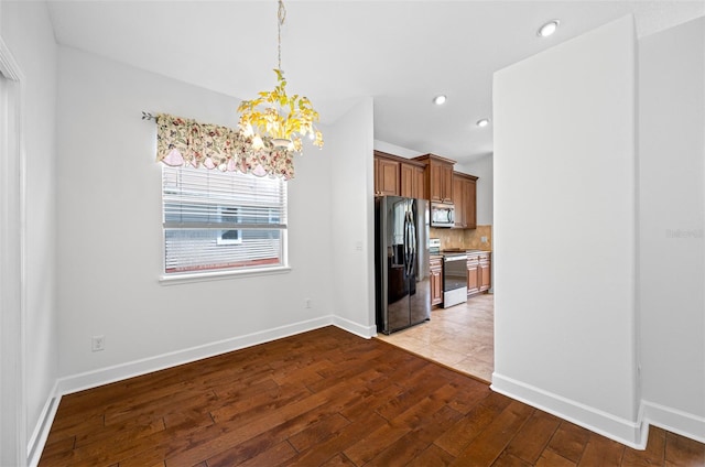 kitchen with pendant lighting, decorative backsplash, appliances with stainless steel finishes, brown cabinetry, and light wood-style floors