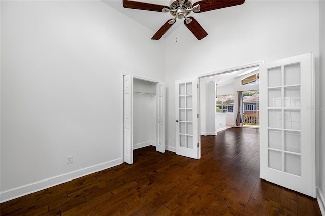 unfurnished bedroom featuring french doors, dark wood finished floors, a closet, high vaulted ceiling, and baseboards