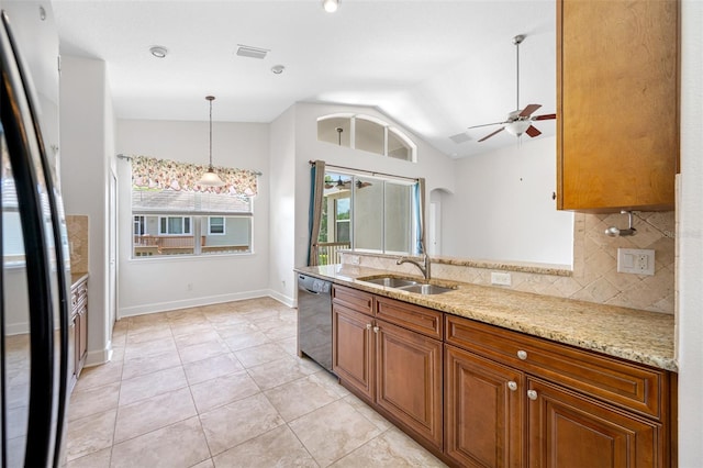 kitchen with brown cabinets, stainless steel dishwasher, freestanding refrigerator, a sink, and light stone countertops