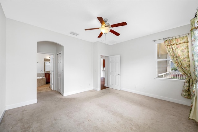 unfurnished bedroom featuring light carpet, baseboards, visible vents, arched walkways, and ensuite bathroom