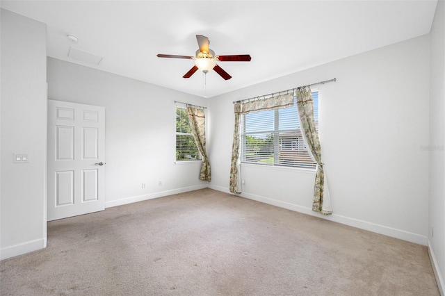 empty room featuring baseboards, a ceiling fan, attic access, and light colored carpet