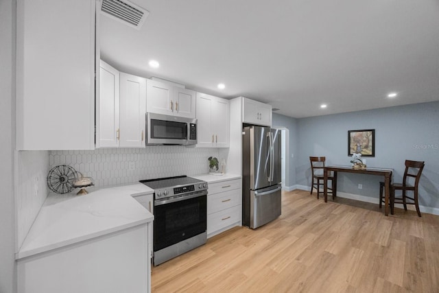 kitchen featuring tasteful backsplash, visible vents, appliances with stainless steel finishes, light wood-style floors, and white cabinetry