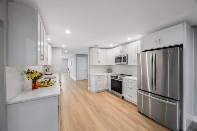 kitchen with stainless steel appliances, light countertops, backsplash, light wood-style flooring, and white cabinets