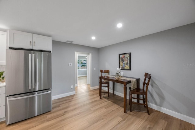 interior space with light wood finished floors, baseboards, white cabinetry, and freestanding refrigerator