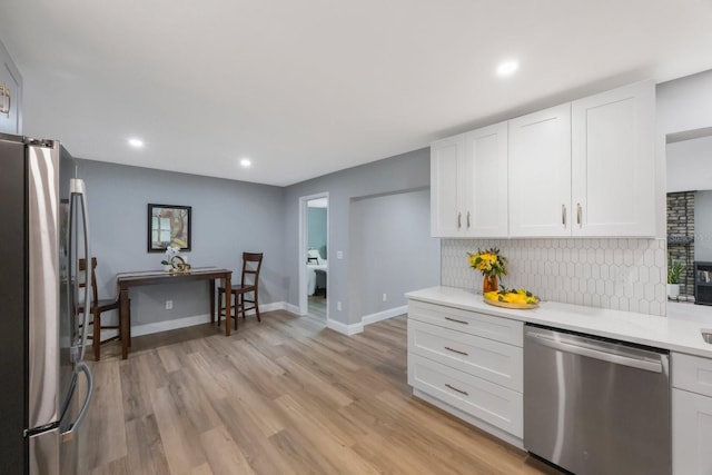 kitchen with white cabinets, decorative backsplash, appliances with stainless steel finishes, light countertops, and light wood-style floors