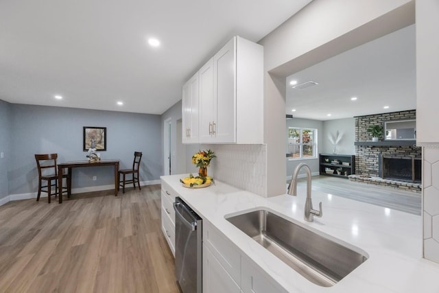 kitchen with a fireplace, a sink, white cabinets, dishwasher, and light wood finished floors