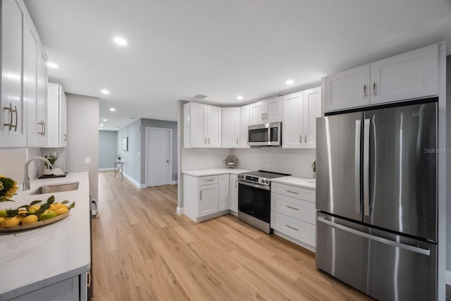 kitchen featuring stainless steel appliances, a sink, light wood-style floors, light countertops, and decorative backsplash