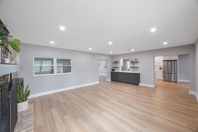 unfurnished living room featuring recessed lighting, a brick fireplace, light wood-style flooring, and baseboards