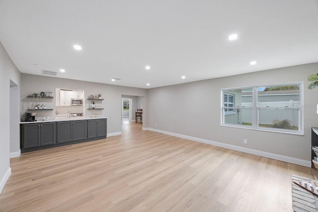 unfurnished living room featuring baseboards, light wood-type flooring, a sink, and recessed lighting