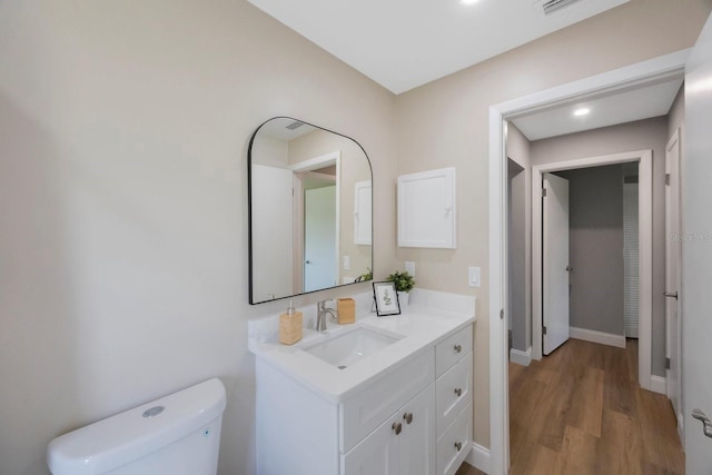 half bath with toilet, baseboards, wood finished floors, and vanity