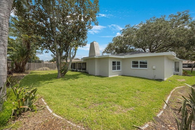 back of property featuring stucco siding, a chimney, fence, and a yard