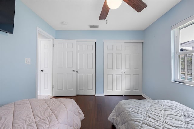 bedroom featuring baseboards, visible vents, dark wood finished floors, ceiling fan, and multiple closets