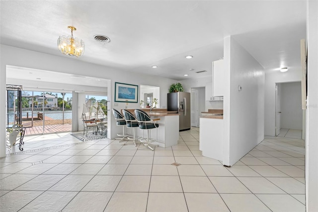 kitchen with light tile patterned floors, white cabinetry, a notable chandelier, a water view, and stainless steel fridge with ice dispenser