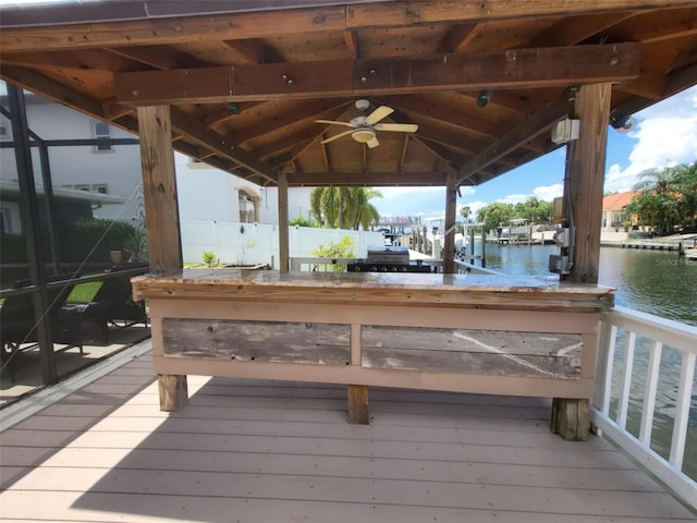 wooden deck featuring ceiling fan, a dock, and a water view