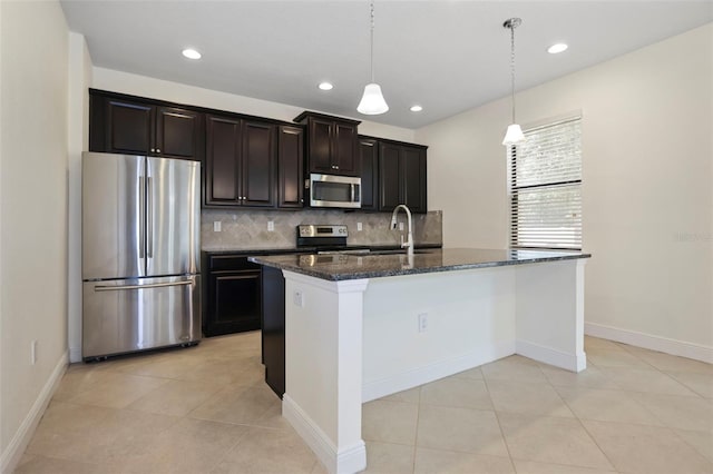 kitchen with dark stone counters, appliances with stainless steel finishes, a sink, a kitchen island with sink, and backsplash