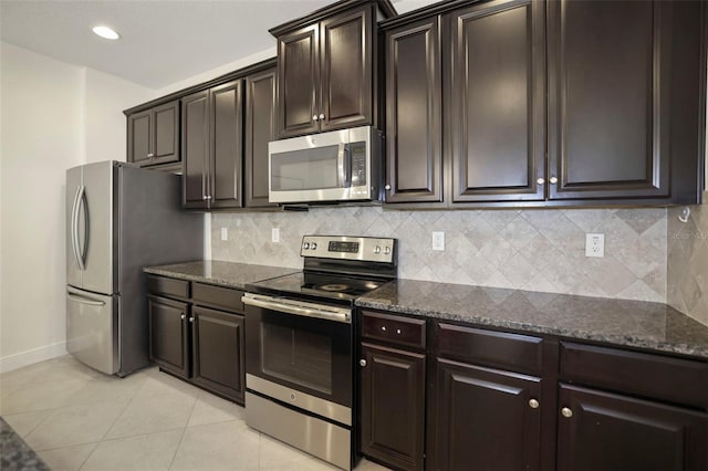 kitchen with appliances with stainless steel finishes, light tile patterned floors, dark stone countertops, and tasteful backsplash