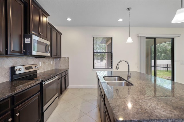 kitchen with a sink, appliances with stainless steel finishes, decorative backsplash, dark stone counters, and a center island with sink