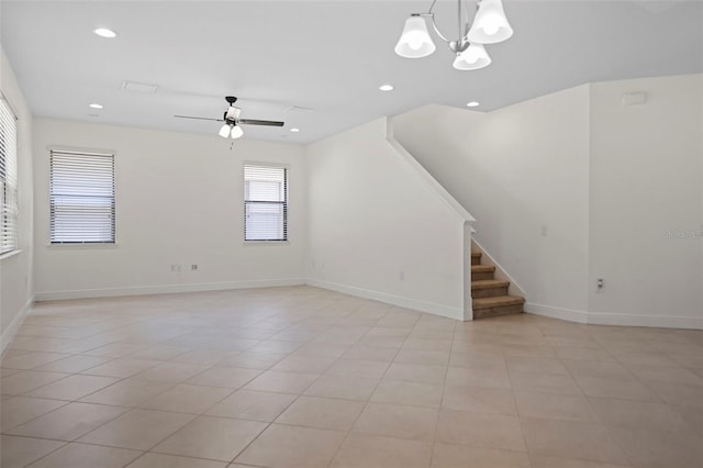 unfurnished living room with ceiling fan with notable chandelier, recessed lighting, baseboards, and stairs