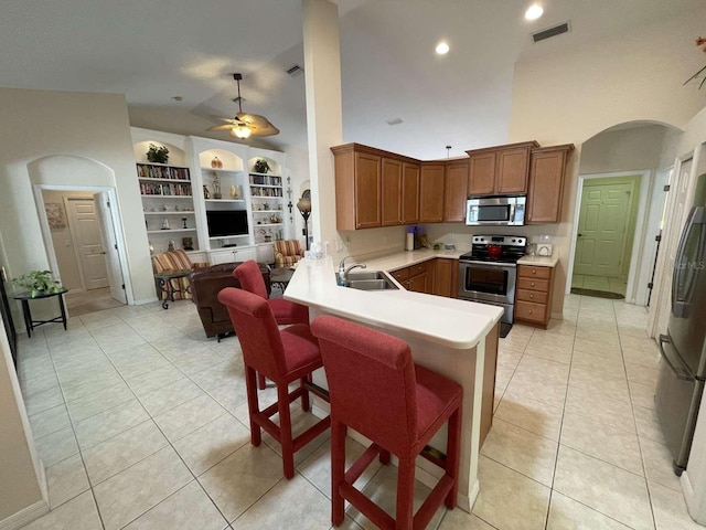 kitchen with appliances with stainless steel finishes, a breakfast bar, kitchen peninsula, sink, and ceiling fan