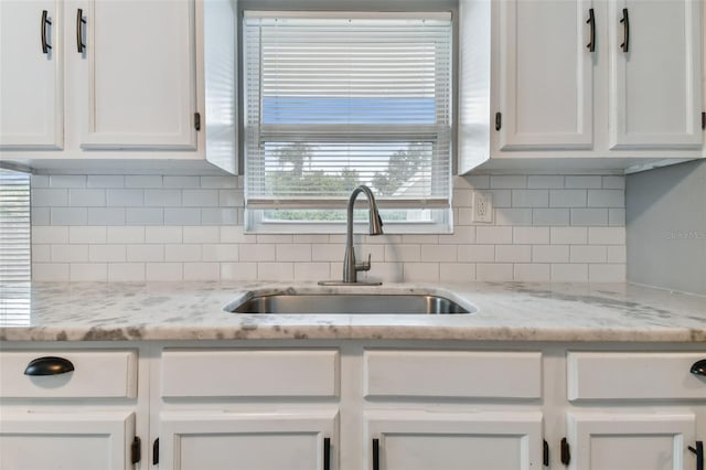 kitchen featuring sink, light stone counters, white cabinets, and tasteful backsplash