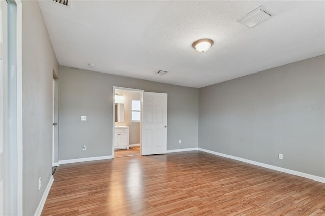 unfurnished bedroom with a textured ceiling, light hardwood / wood-style floors, and ensuite bath