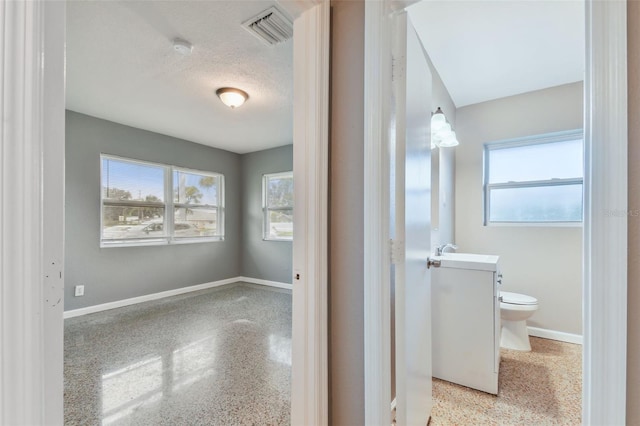 bathroom featuring a textured ceiling, toilet, a healthy amount of sunlight, and sink