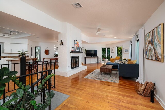 living room with ceiling fan, light hardwood / wood-style floors, a healthy amount of sunlight, and a fireplace