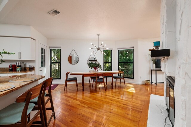 kitchen with white cabinets, hanging light fixtures, light hardwood / wood-style flooring, light stone countertops, and a chandelier