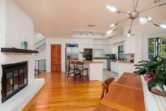 kitchen featuring white cabinets, black appliances, a stone fireplace, light wood-type flooring, and a kitchen bar