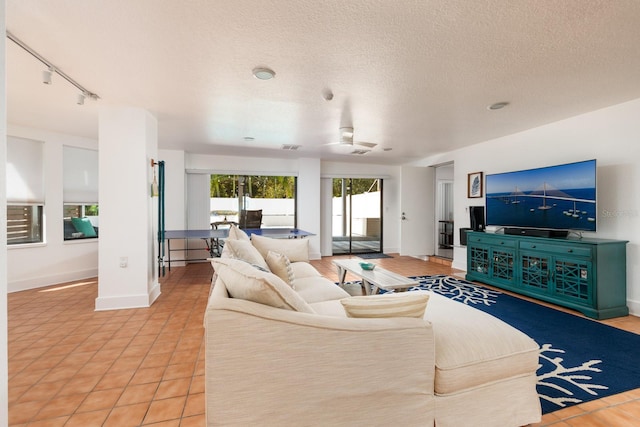 living room with ceiling fan, track lighting, light tile patterned flooring, and a textured ceiling