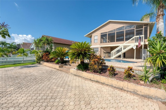 view of front of home with a sunroom, stairway, fence, a patio area, and stucco siding