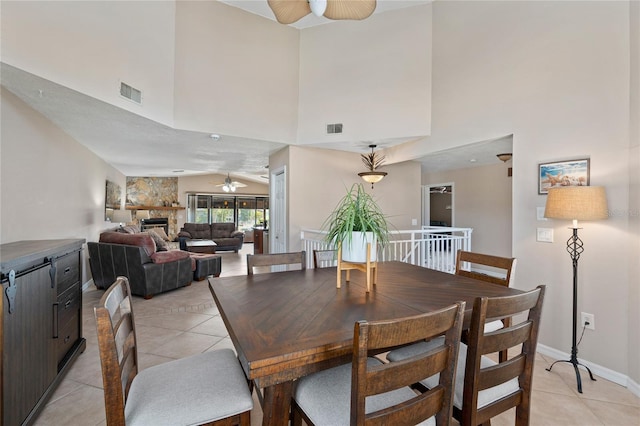 dining space featuring light tile patterned floors, ceiling fan, a stone fireplace, and visible vents