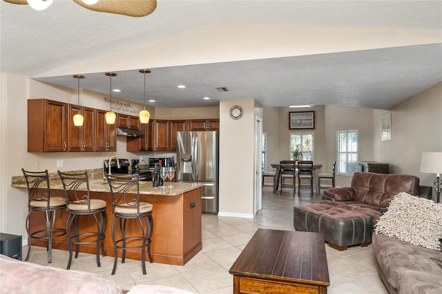 kitchen with lofted ceiling, light stone counters, a peninsula, open floor plan, and stainless steel fridge with ice dispenser