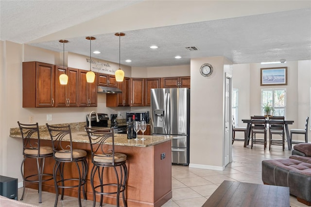 kitchen featuring light stone counters, under cabinet range hood, stainless steel appliances, a peninsula, and visible vents