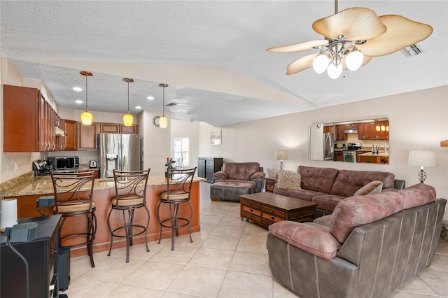 living room with ceiling fan, a textured ceiling, light tile patterned flooring, visible vents, and vaulted ceiling